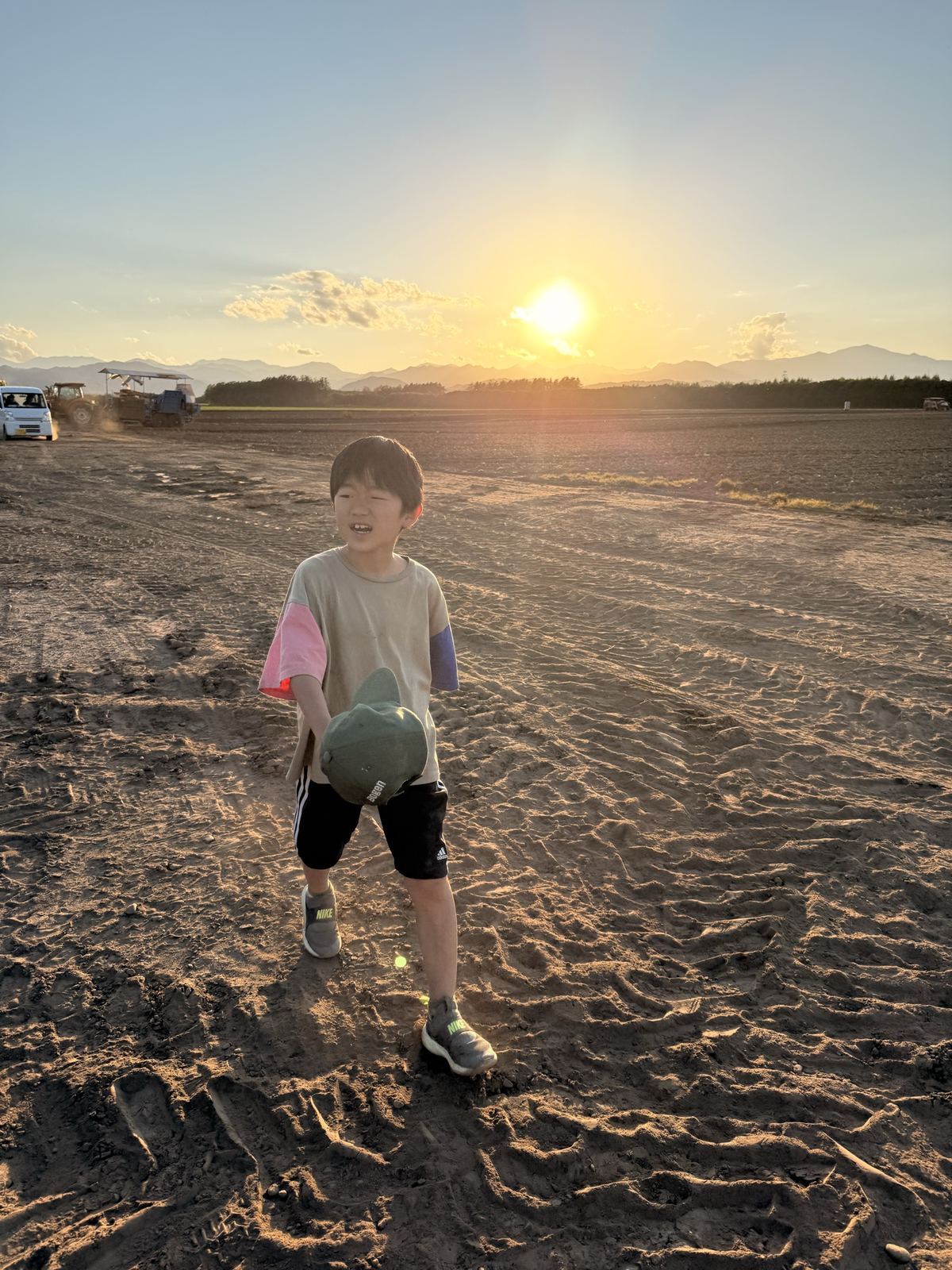 収穫を終え、日高山脈に沈む夕陽を背に畑を歩く小学生
